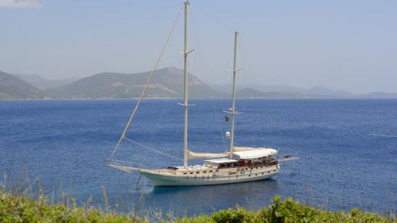 The gulet Liberte 11 is peacefully anchored in blue waters with mountain scenery in the background.